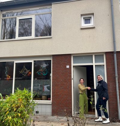 Bewoners staan bij de voordeur van een gerenoveerde woning in een rij huizen.