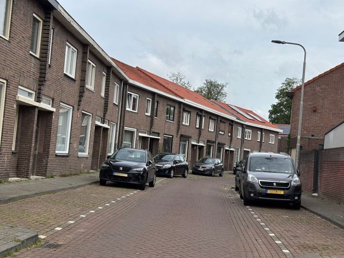 Verduurzaming van rijwoningen met vernieuwde daken en zonnepanelen langs woonstraat met geparkeerde auto's