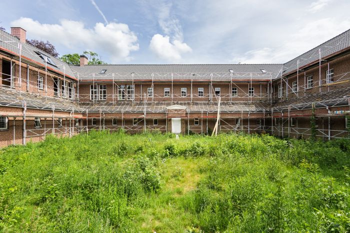 Binnenplaats van bakstenen gebouw met steigers rondom en begroeid binnenterrein tijdens renovatie