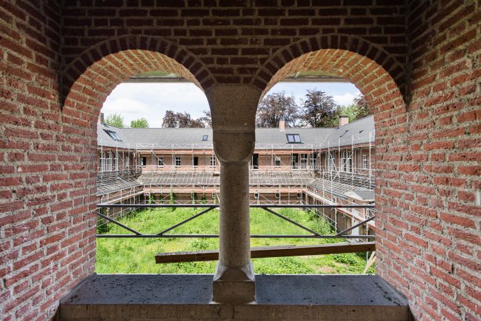Bakstenen galerij met bogen en uitzicht op steigers rond begroeide binnentuin tijdens renovatie
