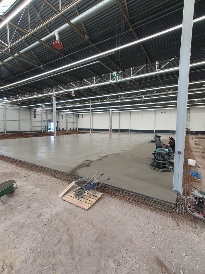 Giet- en afwerkfase van de nieuwe betonvloer in hal A50 bij DAF Eindhoven, met vlindermachines die de verse betonplaat afwerken in de fabriekshal.