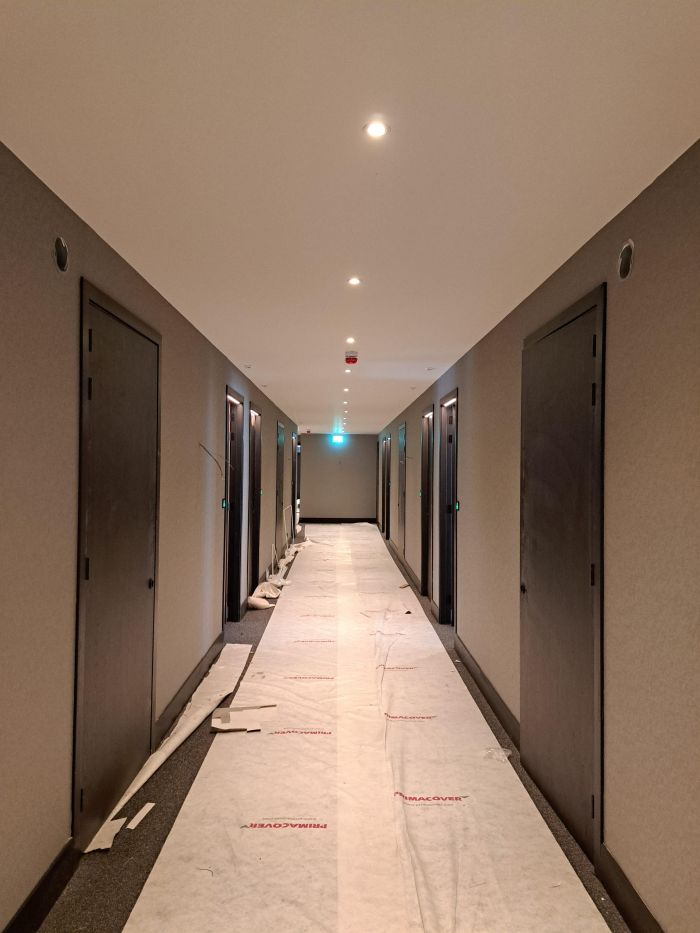 Uitbreiding en renovatie Van der Valk Hotel Wassenaar – hotelgang in afbouw met schilderklare wanden, nieuwe deuren en beschermfolie over de vloer, spotverlichting aan het plafond.