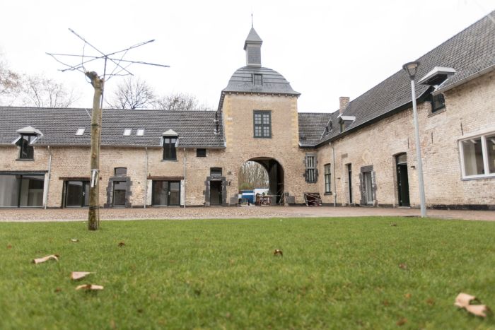Binnenplaats carréhoeve met poortgebouw en klokdak, gezien over een groen gazon — herbestemming tot appartementen, Maastricht.