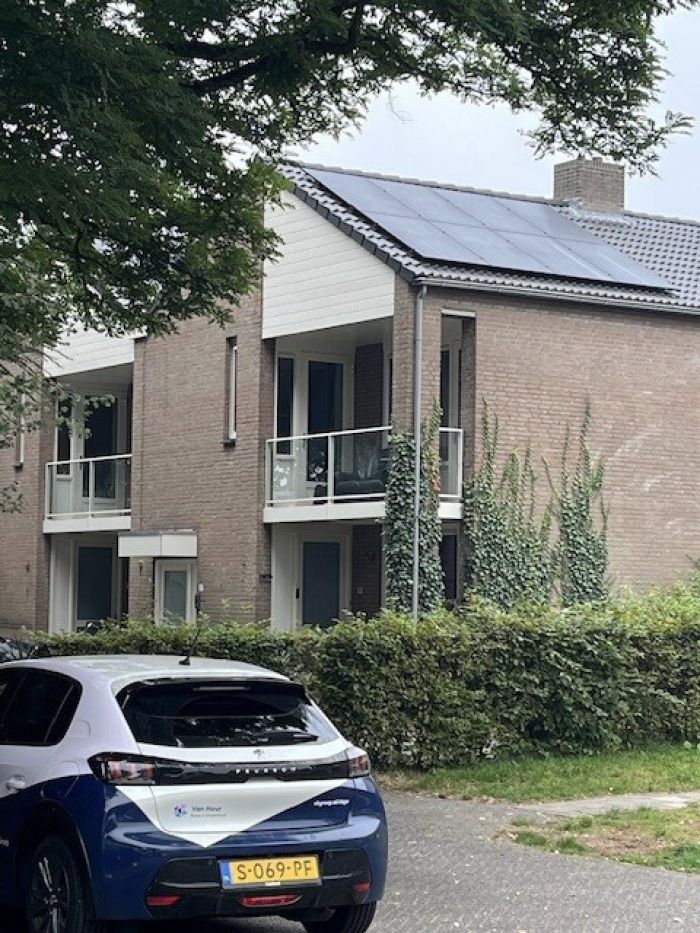Appartementen/maisonnettes in Stramproy (groot onderhoud) met bakstenen gevel, wit topgeveldeel en balkons met glazen balustrades; op het schuine dak liggen zonnepanelen. Voor het gebouw staan een haag en een geparkeerde bedrijfsauto.