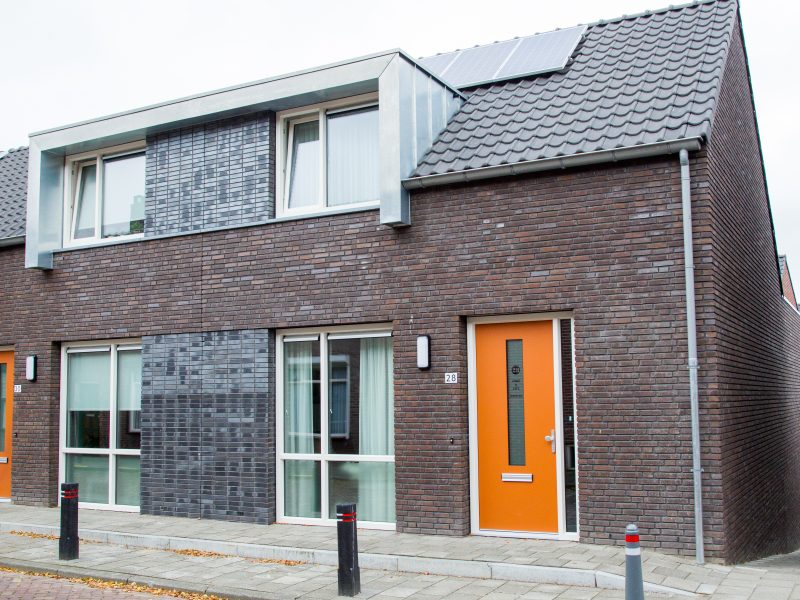 Nieuwbouwwoningen in Zevenbergen met rode en donkergrijze bakstenen gevels, opvallende oranje voordeuren en moderne zinken dakkapellen