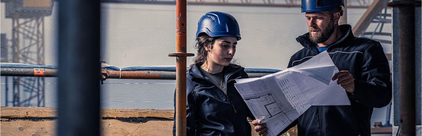 “Twee bouwmedewerkers met blauwe helmen bekijken bouwtekeningen op een bouwplaats.